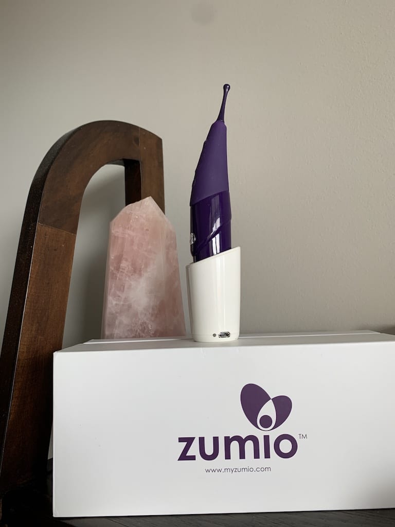 Zumio X stands in its charger. It is a purple vibrator that resembles a pen.