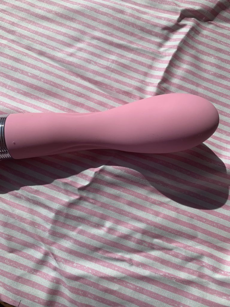 The pillow talk sassy vibrator is a soft pink displayed on a pink and white striped piece of cloth. It is a g-spot vibrator and it's curved head reflects that. 